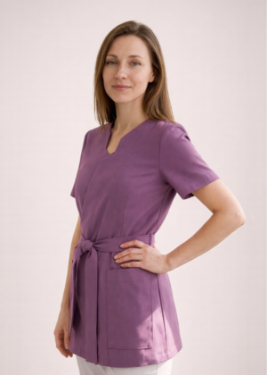 NOWA! TUNIKA MEDYCZNA – KOPERTOWA Nasza tunika przeszła prawdziwą metamorfozę – uwzględniliśmy wszystkie opinie naszych klientek, aby stworzyć model jeszcze lepszy i bardziej komfortowy w codziennej pracy. Nowa tunika nie rozchodzi się na biuście, dzięki czemu zapewnia pełną swobodę ruchów i komfort podczas pracy z pacjentem. Głębsze założenie na biuście sprawia, że nie ma potrzeby zakładania dodatkowego trykotu, a rezygnacja z mało estetycznych zatrzasków gwarantuje perfekcyjne ułożenie materiału. Wiązanie w talii pozwala dopasować tunikę do każdej sylwetki, podkreślając kobiece kształty i jednocześnie dbając o wygodę przez cały dzień. Pionowe cięcia wysmuklają sylwetkę, nadając całości eleganckiego charakteru. Dodatkowym atutem są trzy praktyczne kieszenie, w tym jedna zaprojektowana specjalnie na telefon. Poznaj i pokochaj naszą nową tunikę – stworzoną z myślą o Tobie!
